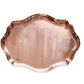 A scalloped copper serving tray with embossed floral patterns, photographed from directly above on a textured white fabric background.