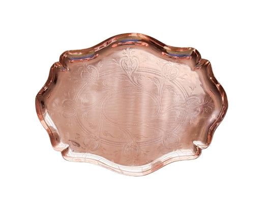 A scalloped copper serving tray with embossed floral patterns, photographed from directly above on a textured white fabric background.
