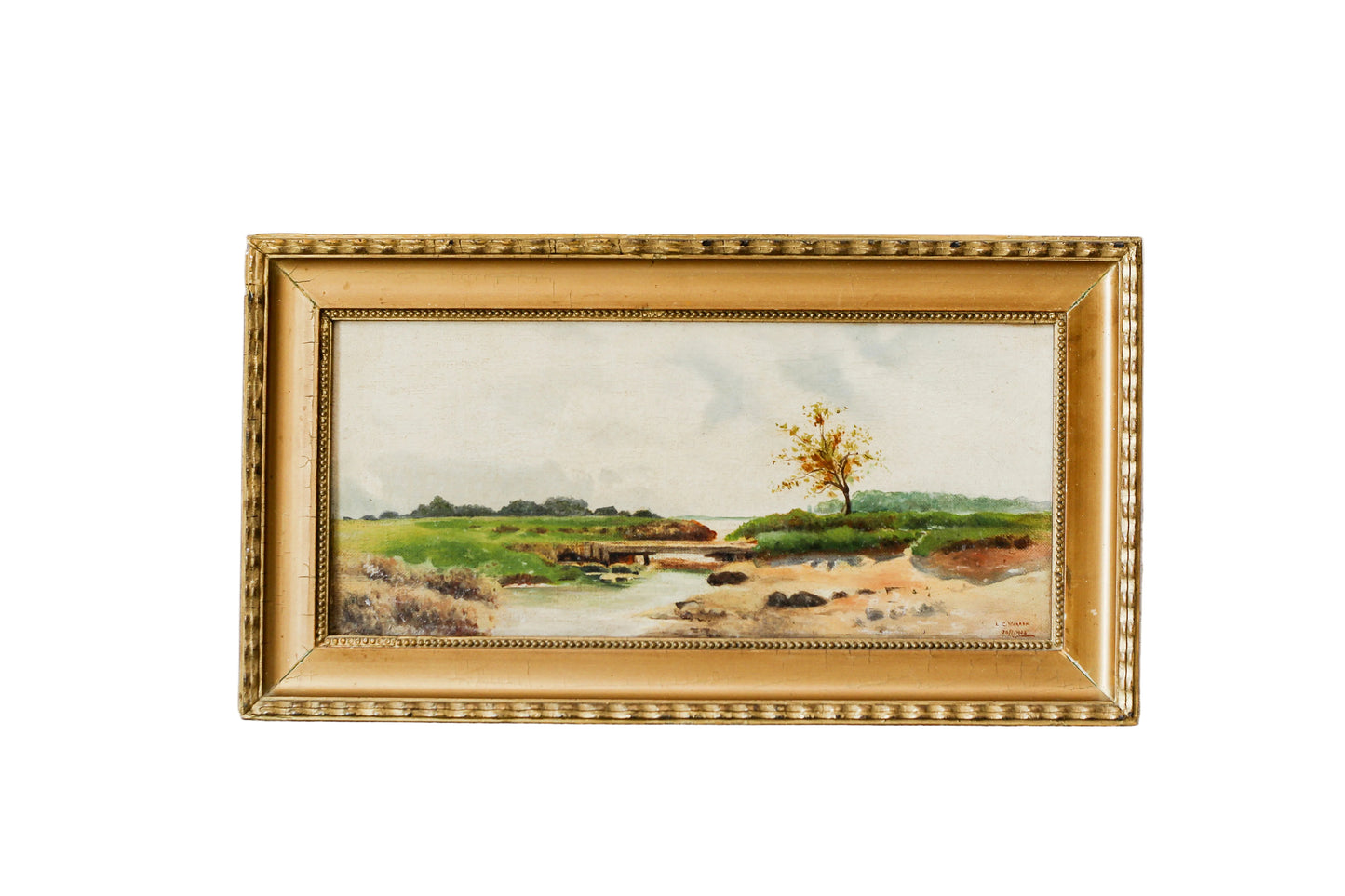 A framed landscape oil painting featuring a river, green fields, and a single tree, housed in an ornate gold frame, set against a textured white wall.