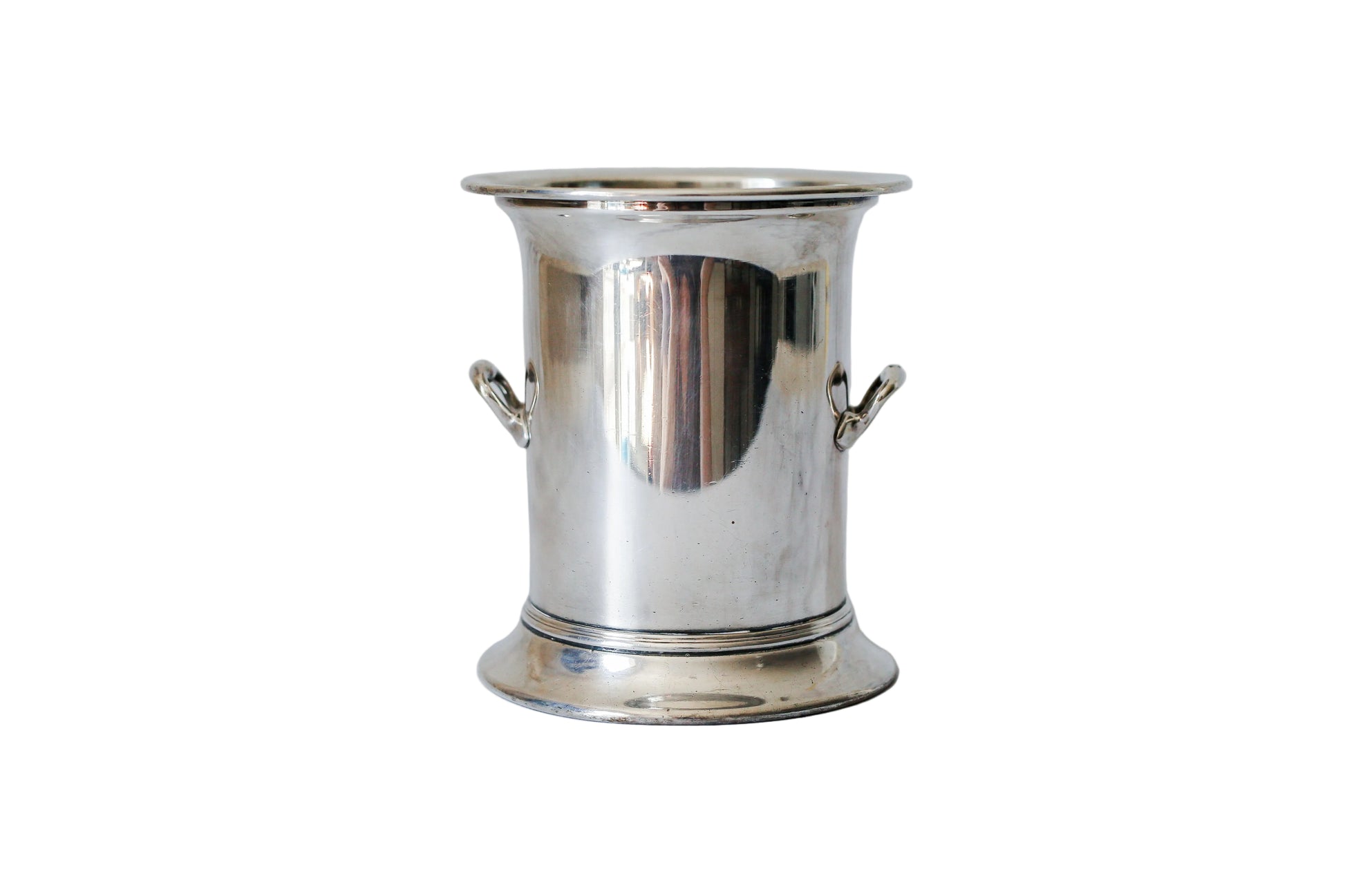 A polished silver metal bucket or ice bucket with side handles, standing on a white marble surface against a matching marble background.