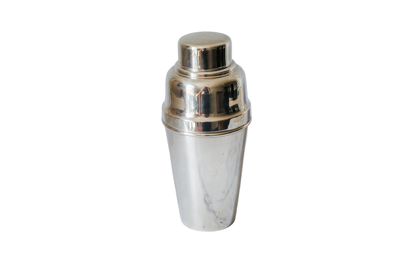 A polished silver metal cocktail shaker standing upright on a white marble surface with a matching marble background.