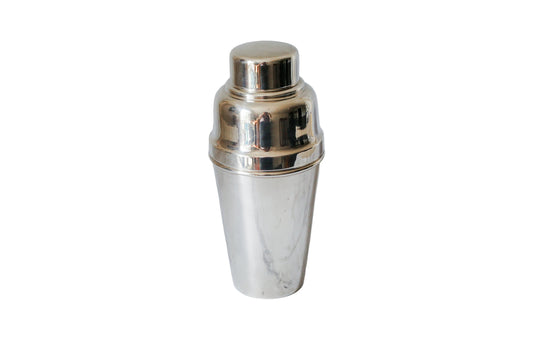 A polished silver metal cocktail shaker standing upright on a white marble surface with a matching marble background.
