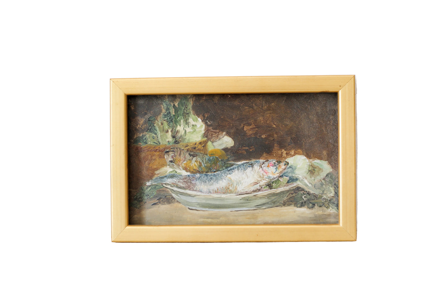 A framed still life oil painting depicting a fish on a plate, housed in a light natural wood frame and leaning against a textured off-white plaster wall.