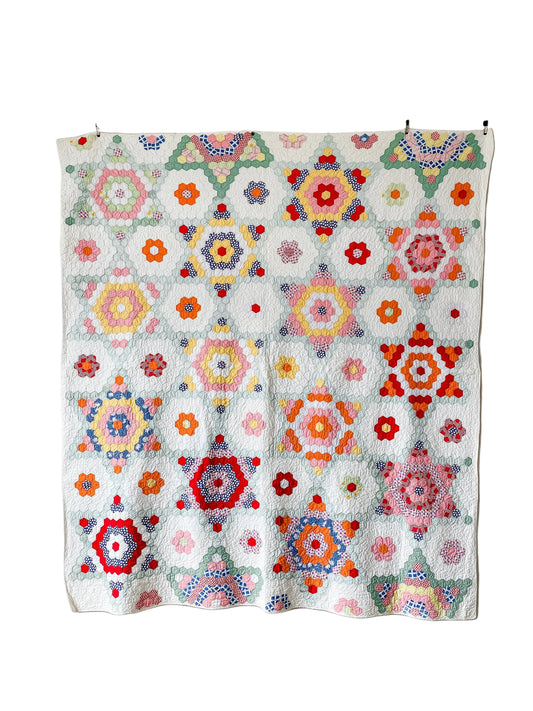 Colorful geometric patterned quilt hanging on a rack against a white wall.