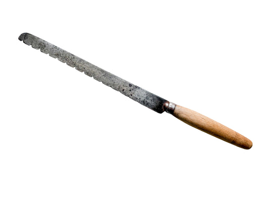 A vintage serrated bread knife with a long, weathered steel blade and a light brown wooden handle, resting diagonally on a textured off-white fabric background.
