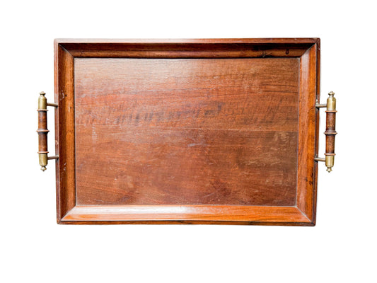 A rectangular wooden serving tray with a warm reddish-brown finish and two brass-and-wood handles, shown against a white textured fabric background.