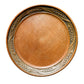 A round wooden serving platter with a smooth, polished brown center and a carved decorative border featuring wheat stalks, shown from a top-down view on a light gray textured background.
