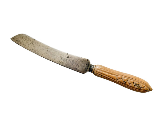 Old bread knife with a wooden handle on a light wooden surface