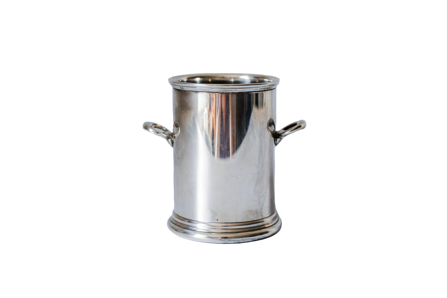 A small polished silver metal pot with side handles, standing on a white marble surface against a matching marble background.