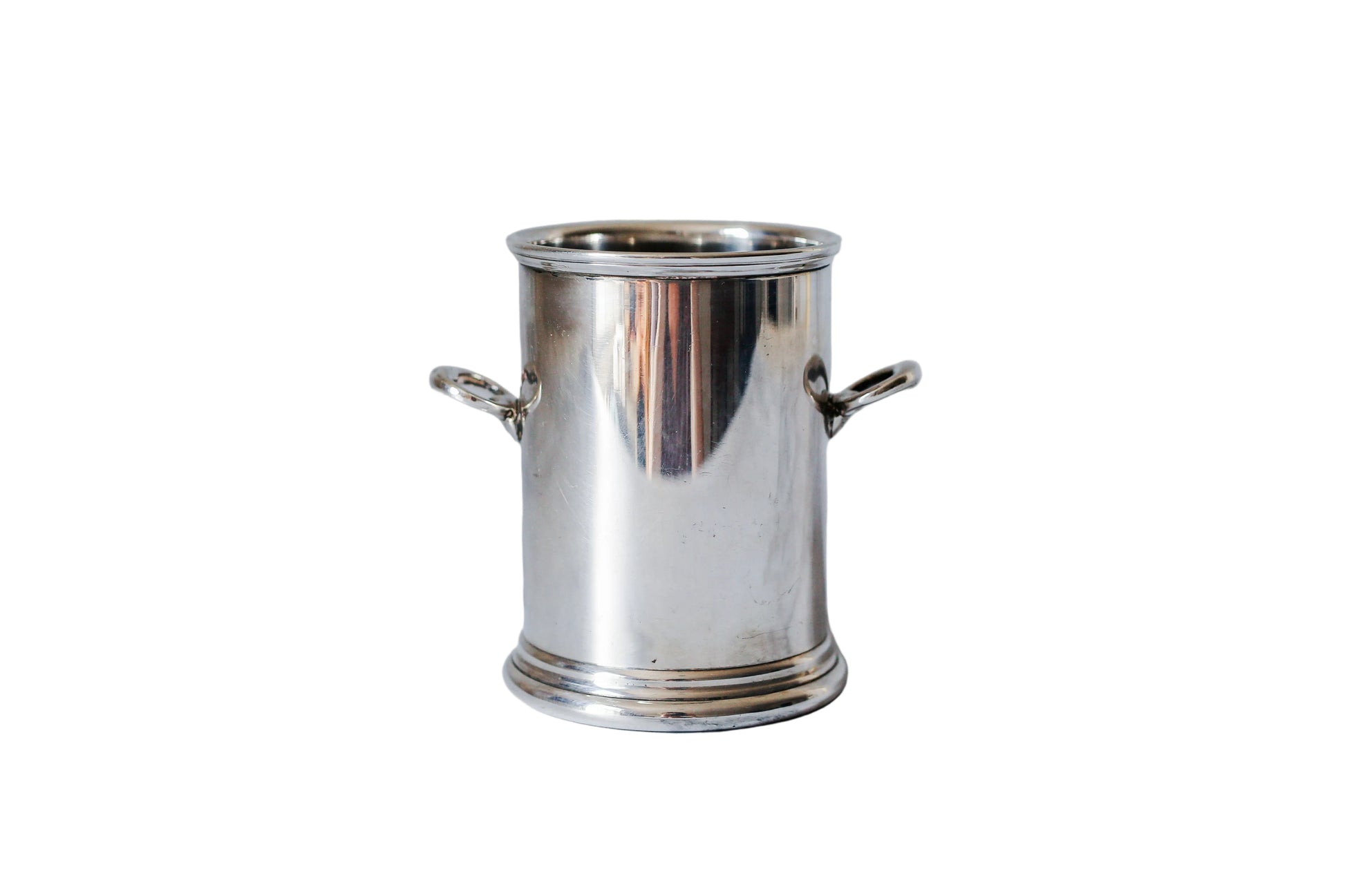 A small polished silver metal pot with side handles, standing on a white marble surface against a matching marble background.
