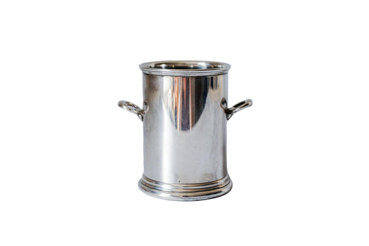 A small polished silver metal pot with side handles, standing on a white marble surface against a matching marble background.
