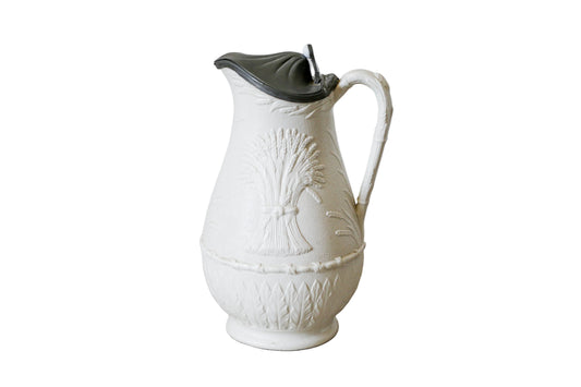White ceramic pitcher with black lid on a textured surface