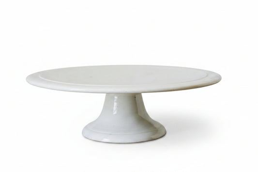 White ceramic cake stand on a marble surface with a light gray background