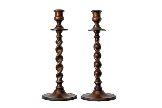 Two wooden candlesticks with twisted design on a textured wall background