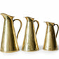 Three brass pitchers of varying sizes on a textured surface with a light background