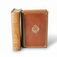 Two ornate leather-bound books on a light wooden surface with a white background