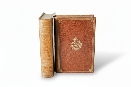 Two ornate leather-bound books on a light wooden surface with a white background