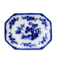 An octagonal white porcelain serving platter with blue hand-painted floral and landscape motifs, set against a textured, distressed off-white wall.