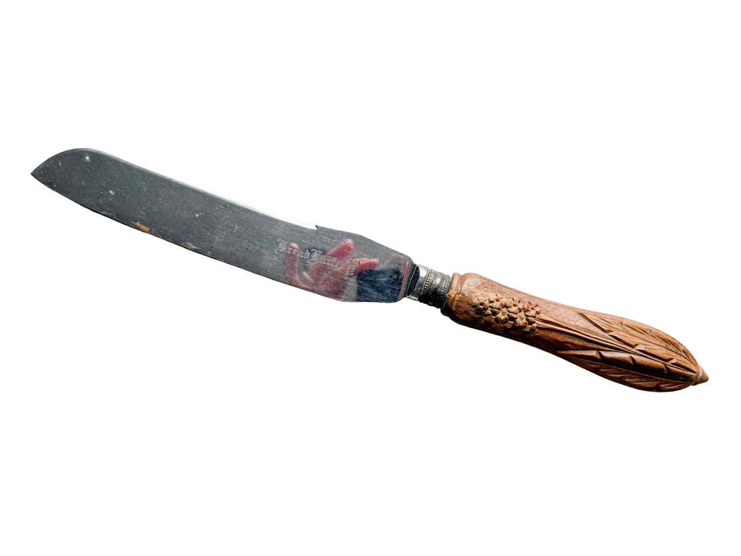 A vintage wooden-handled knife with a dark metal blade, featuring a carved wood handle and a red painted section near the base of the blade, displayed on a textured off-white fabric background.