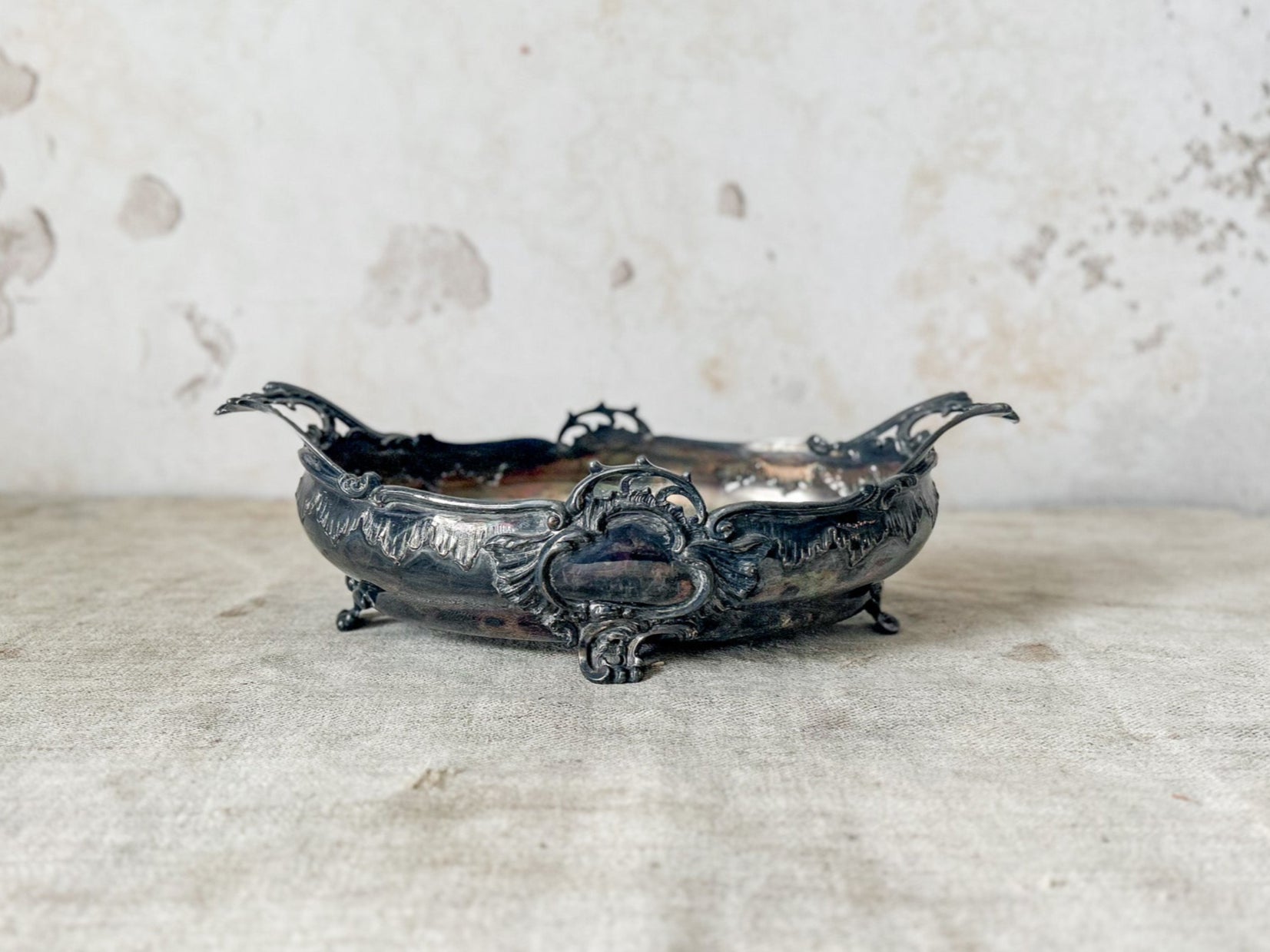 Decorative silver bowl on a textured surface with a distressed wall background