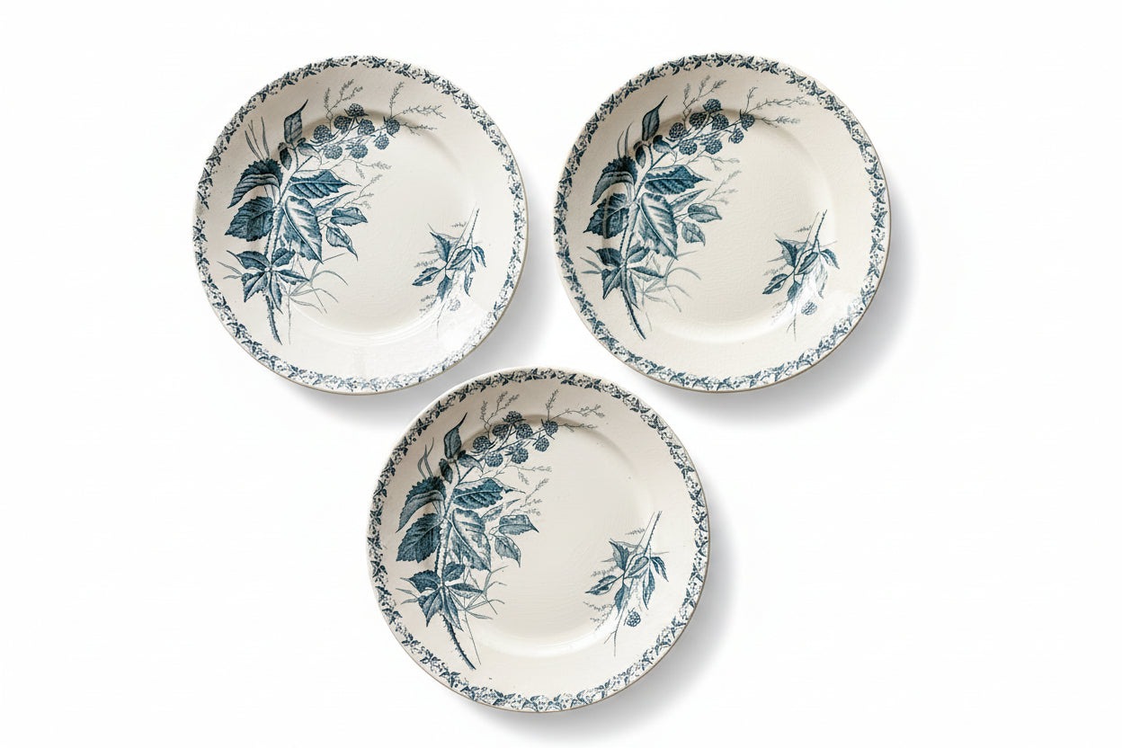 Three ceramic plates with blue leaf patterns on a beige fabric background