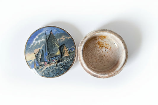 Ceramic dish with a painted lid featuring a sailboat on a textured surface