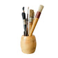 Set of paintbrushes in a wooden holder on a rustic wooden surface with a textured white wall background.