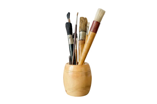 Set of paintbrushes in a wooden holder on a rustic wooden surface with a textured white wall background.
